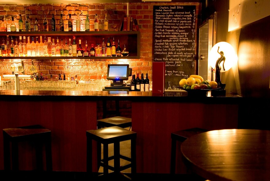 Lamplit bar with stools, glasses, blackboard menu and rows of bottles.