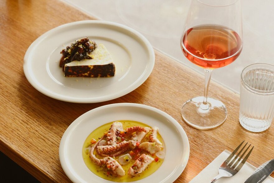 A plate of octopus, cheese and a glass of wine