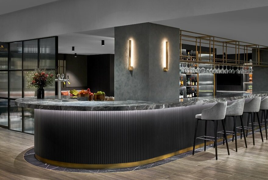 An elegant curved bar in the Melbourne Marriott Hotel, decorated in shades of grey, with high bar stools arranged around the bar.