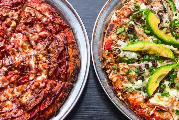 Two pizzas, one with avocado on top.