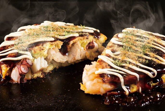 Japanese savoury pancake (okonomiyaki) cooking on a hot griddle, cut in half to show the interior.
