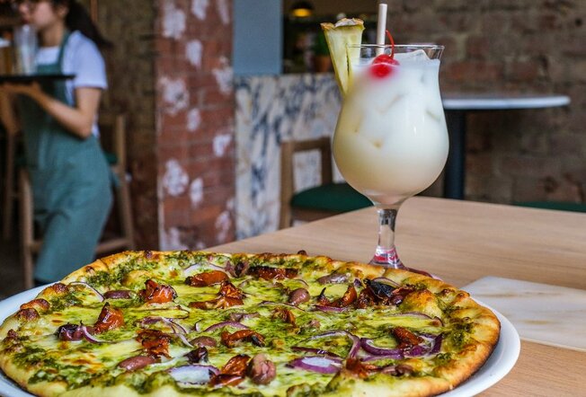 A pizza and a pina colada on a restaurant table.