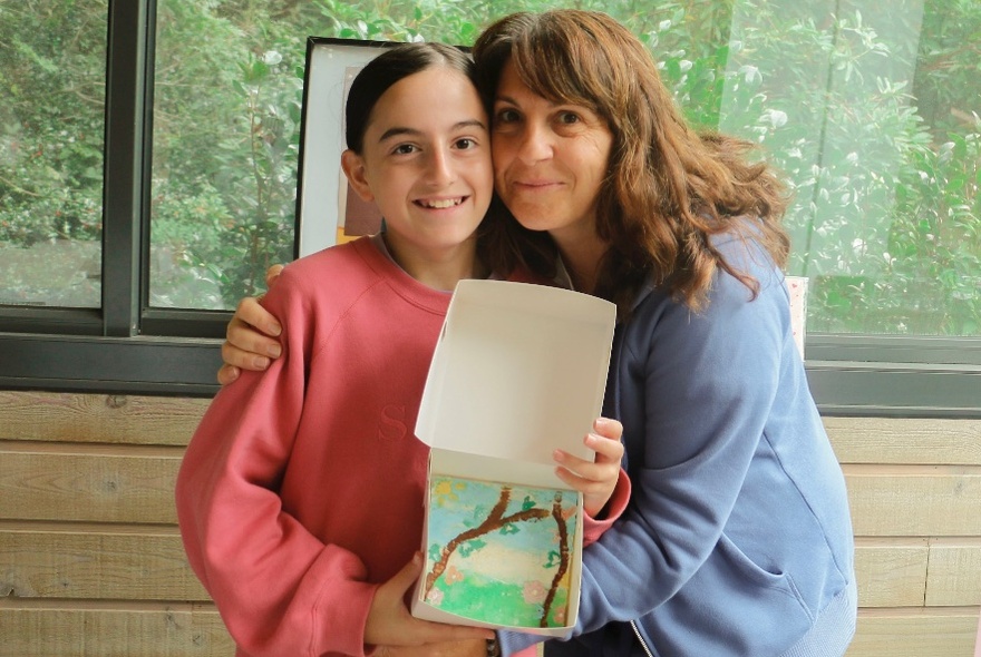 A woman cuddles a child who holds up a painting she had created. 