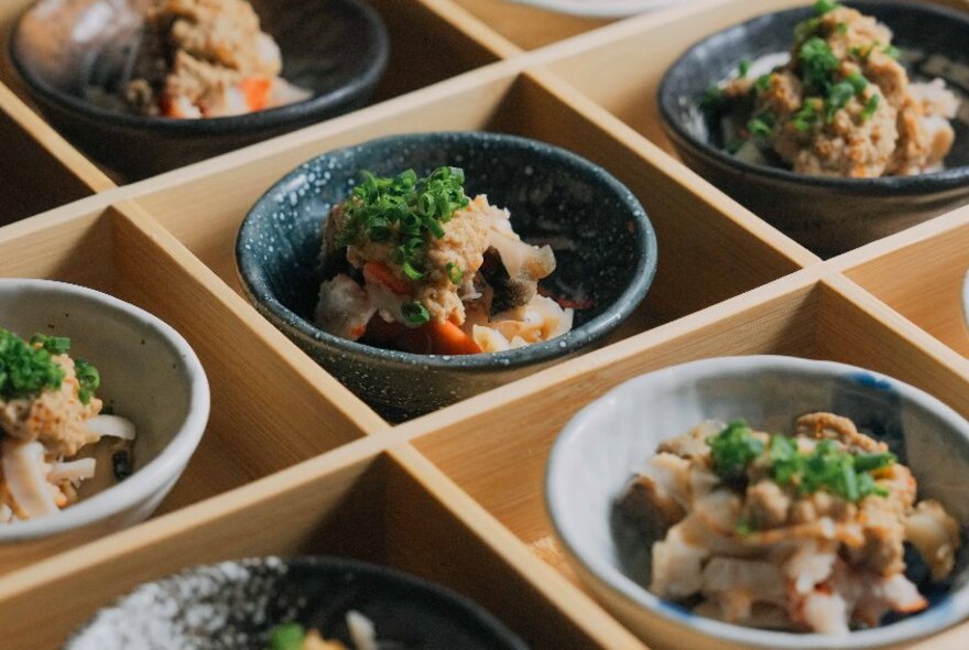 Small bowls of food arranged in a wooden frame.