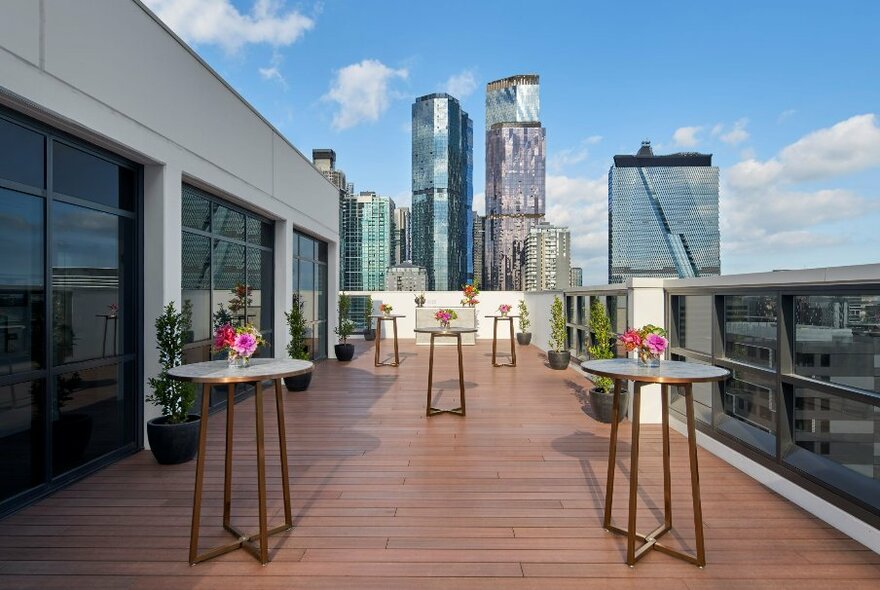 The deck at the Courtyard Melbourne hotel with bar tables and city skyline views.