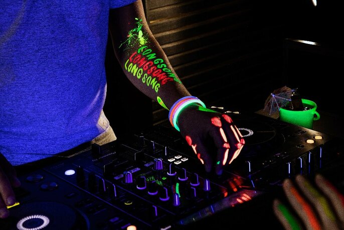 Close up of dj hands on turntable dials, hands and arms decorated with glow in dark paint and bangles.