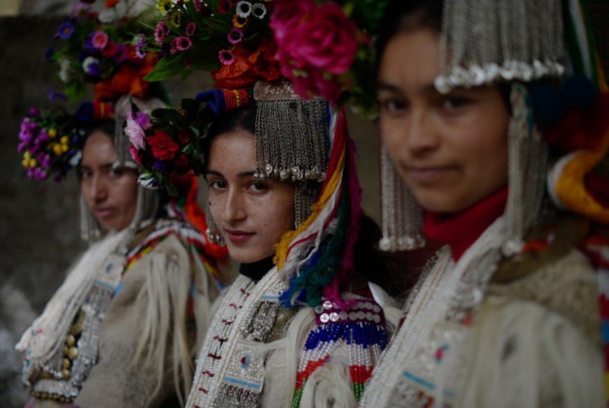 A dark picture of three women from Ladakh in traditional costumes with elaborate headdresses containing flowers and fringing. 
