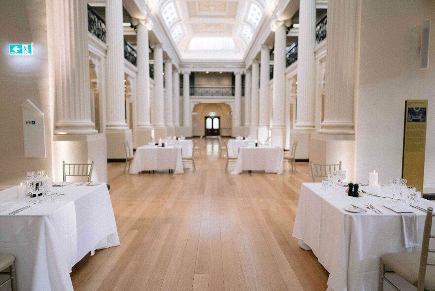 Tables covered in white linen with flowers and candles, arranged in the high-ceilinged Queens Hall at State Library Victoria.