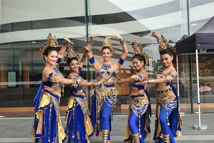 Five women dressed in blue and gold Sri Lankan dancing costumes and headgear posing outdoors.
