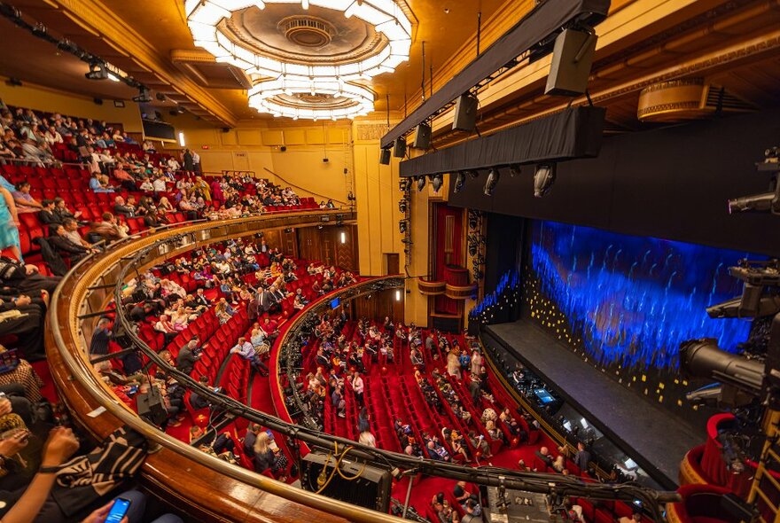 A grand theatre with red seats filling before a show.