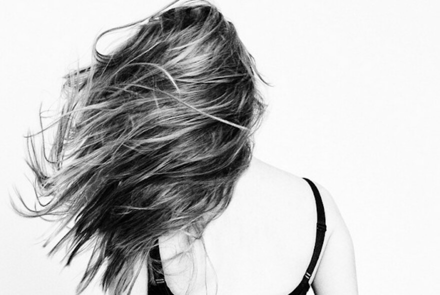 Black and white image of the back of a woman, her long hair tousled and blowing in the wind. 