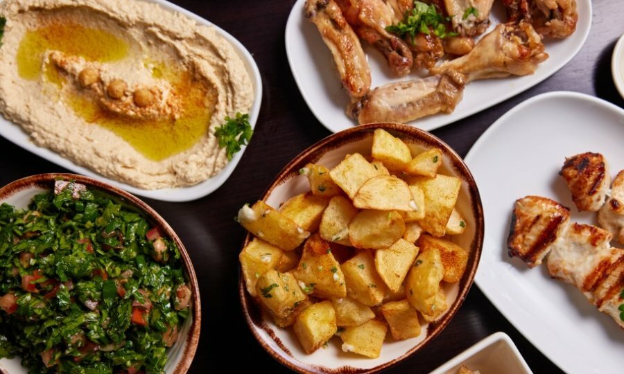 A table set with Lebanese dishes including hummus, tabbouleh, potatoes and chicken.