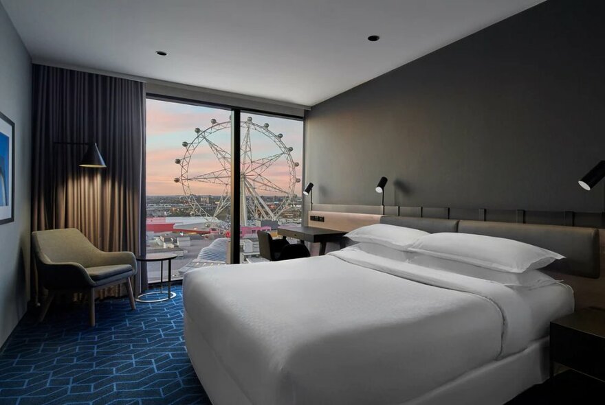 A deluxe room in the Vibe Hotel Docklands in Melbourne, featuring a queen-size bed with white linen, blue carpet and a view of the Melbourne Star.