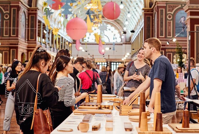 People browsing a designer stall and talking to the stallholder inside the Royal Exhibition Buildings interior.