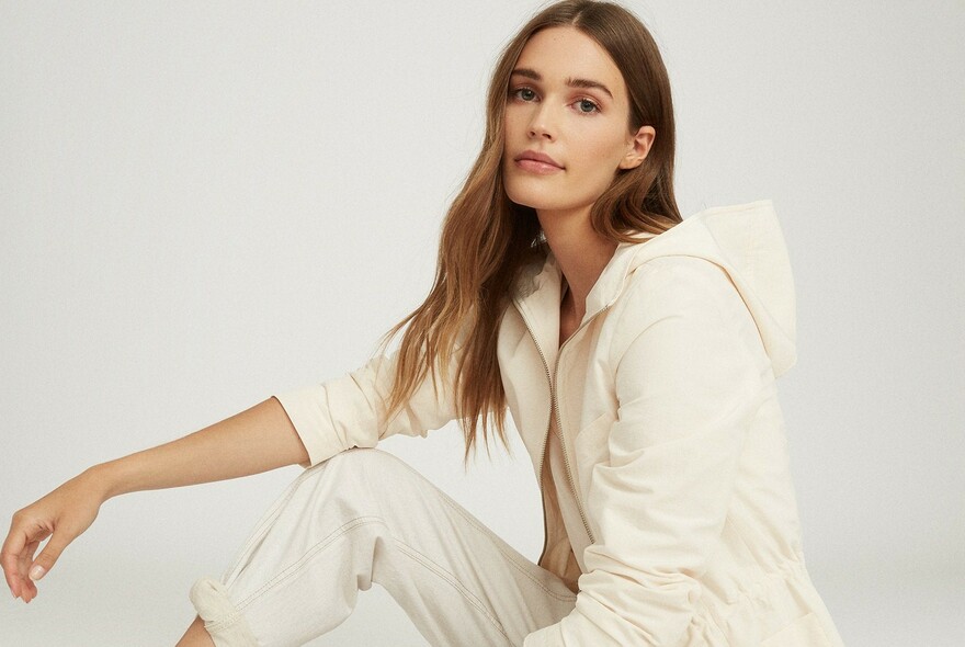 Mode with long, light brown hair in cream hooded jacket and pants.