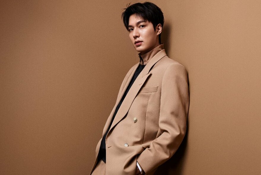 Male model wearing brown suit, leaning against a brown wall.