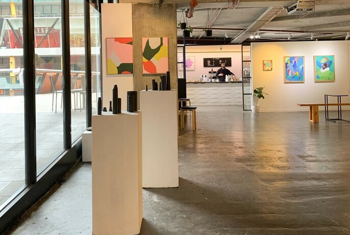 Interior of No Vacancy Gallery showing the exhibition space and artworks and their cafe visible in the background.