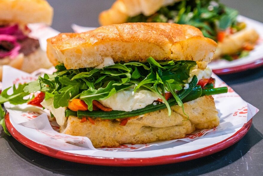 A focaccia sandwich with cheese, rocket and peppers in it.