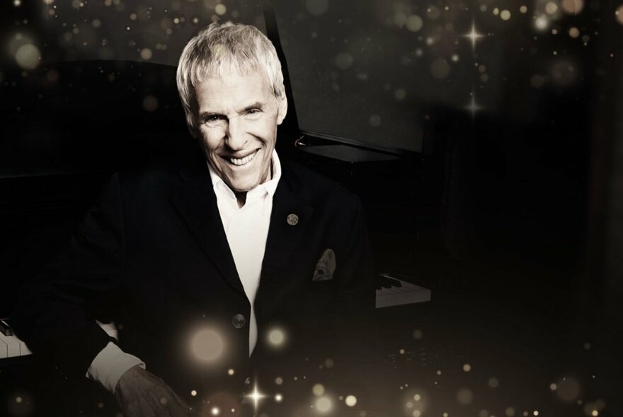 A glamourised black and white portrait of Burt Bacharach in a black suit and white shirt with stars and light bursts around him.