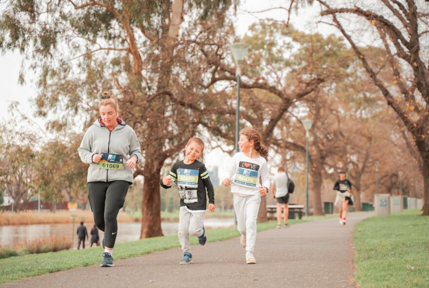 An adult and two children running on a path alongside the Yarra river.