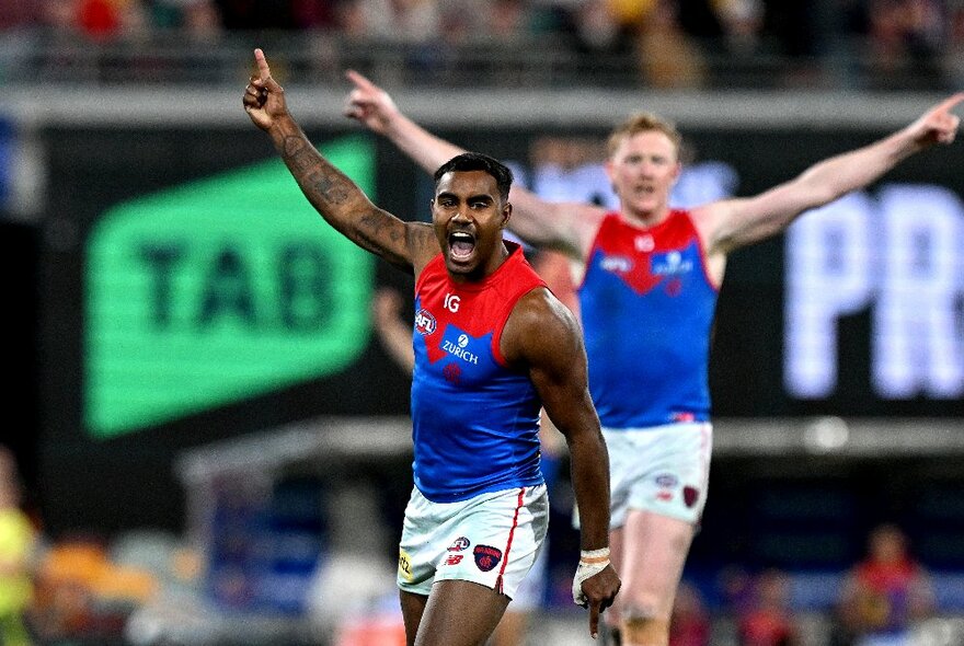 Two Melbourne AFL football players with arms raised during a match.