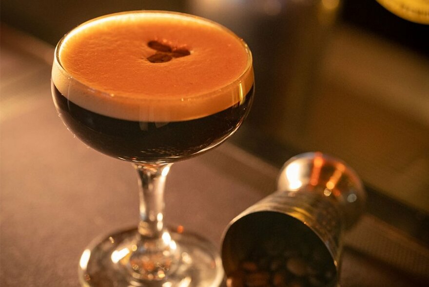 An espresso martini in a shallow glass, resting on a counter.