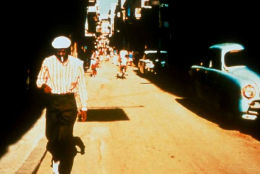 The cover of the Buena Vista Social Club album with man in a flat cap walking down a street in Havana, an iconic Cuban car in the background. 