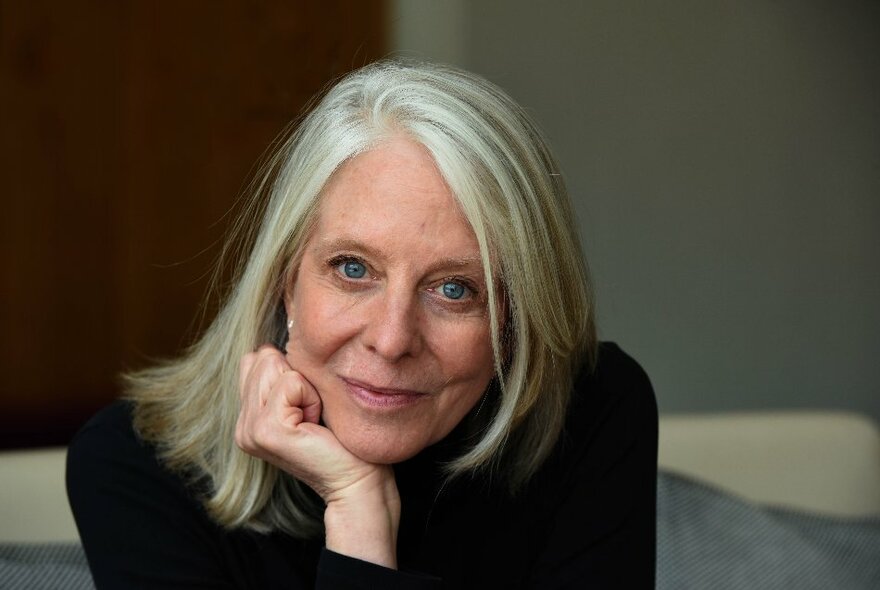 Author Bonnie Garmus, a woman with straight white blond hair in a side part, her chin resting on her folded hand, staring intently at the viewer.