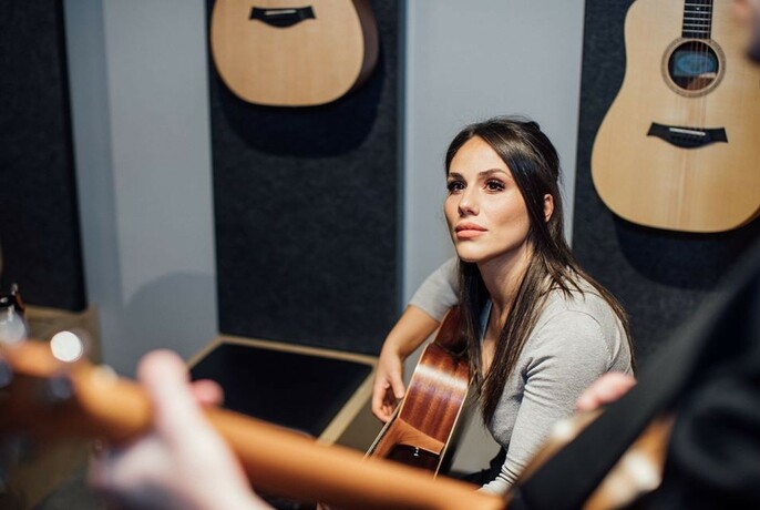 Woman with a guitar listening to an instructor.