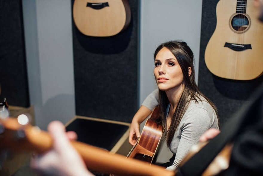 Woman with a guitar listening to an instructor.
