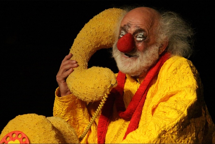 A clown character dressed in yellow, holding a huge yellow telephone.