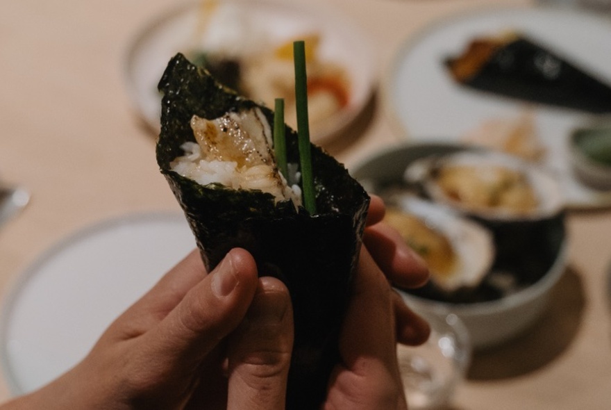 A hand holding temaki sushi, a cone-shaped sushi roll.