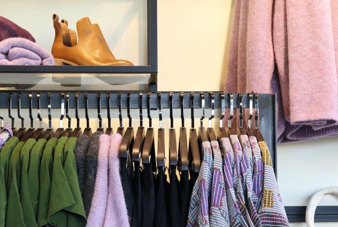 Store display of clothes hanging on a rack and shoes on a wall shelf.