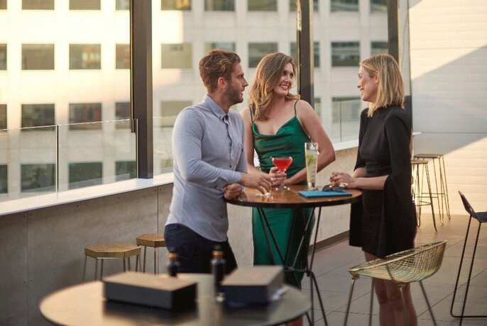 Three people at a rooftop bar talking and drinking.