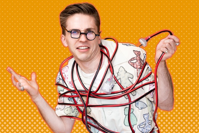 Comedian tied up in red cables, looking bemused, against an orange background.