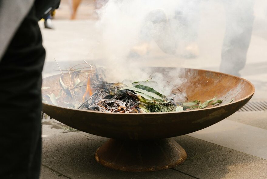 A large shallow bowl of burning leaves and bark at a smoking ceremony. 