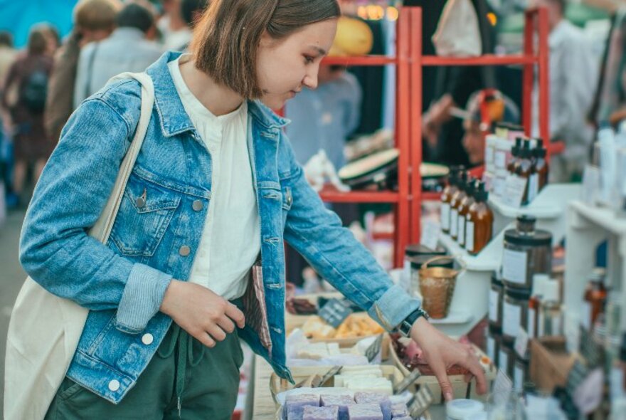 A woman in a denim jacket browsing at a market stall. 