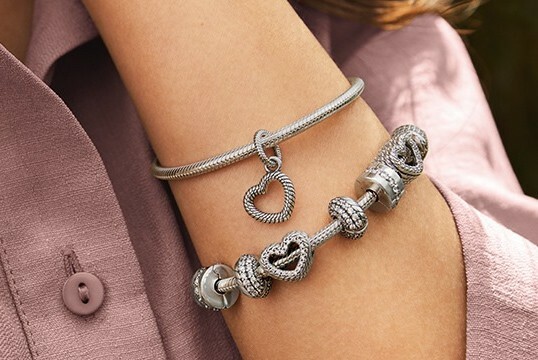 Two silver bracelets on an arm against dusty pink clothing.