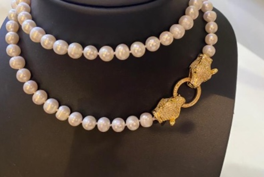 Pearl necklace with a gold clasp displayed on a a head mannequin.