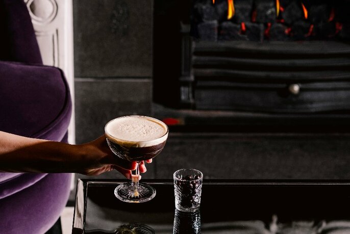 Person enjoying a cocktail by the fire.
