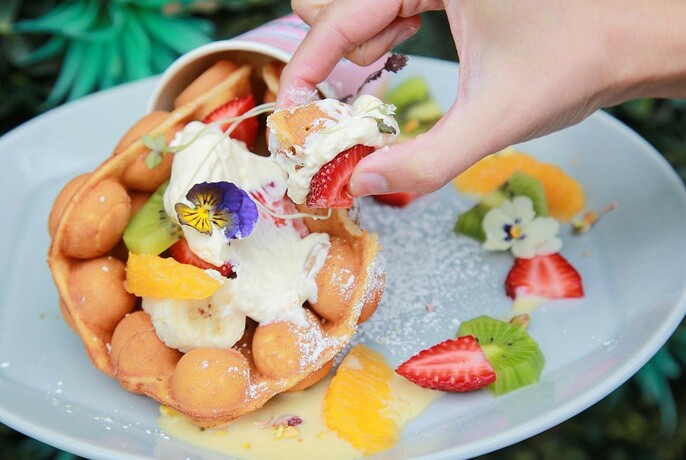 A crepe filled with fruit and cream and a hand taking a small portion. 