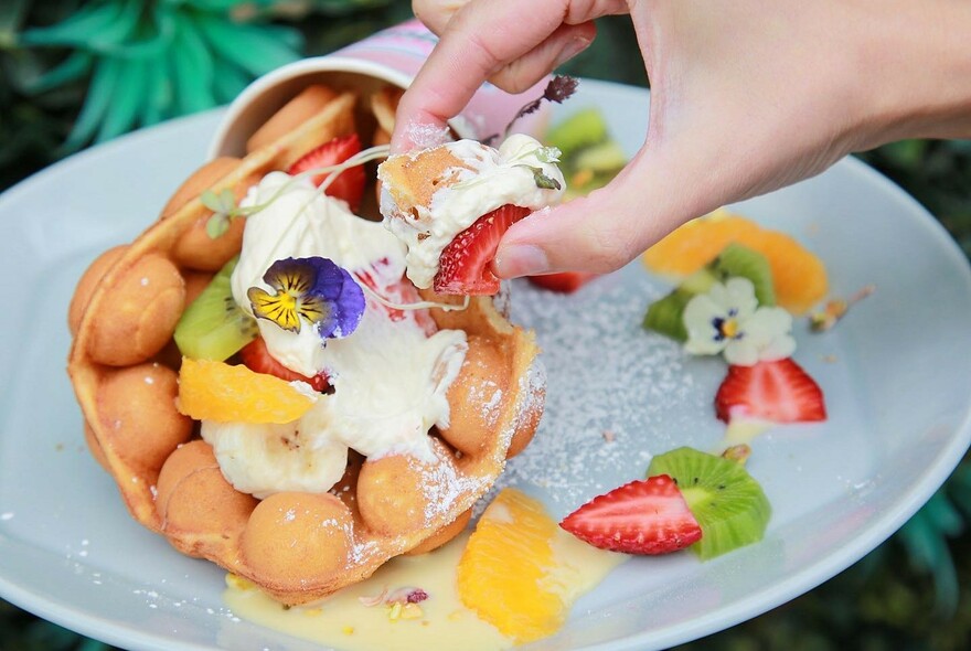 A crepe filled with fruit and cream and a hand taking a small portion. 