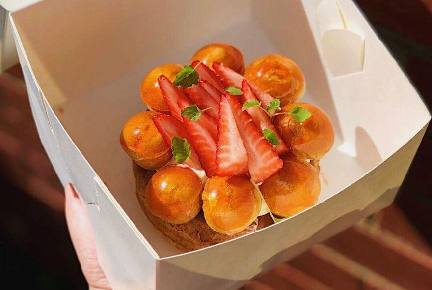 A gourmet cake topped with strawberries in a white takeaway box.