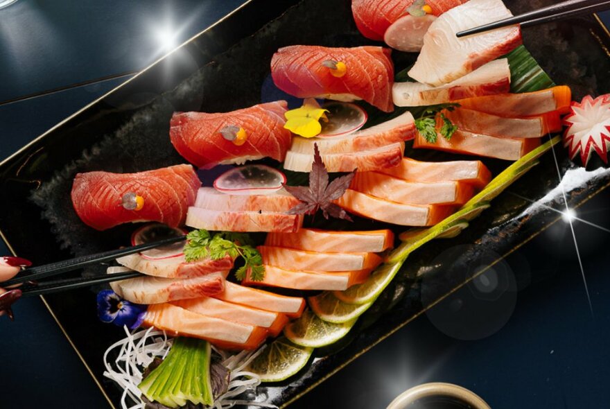 A platter of fresh sashimi with hands using chopsticks to select pieces.