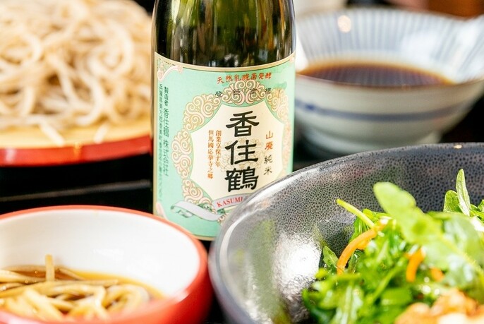 Bowls of ramen with bottle of sake, bean shoots and soy sauce.
