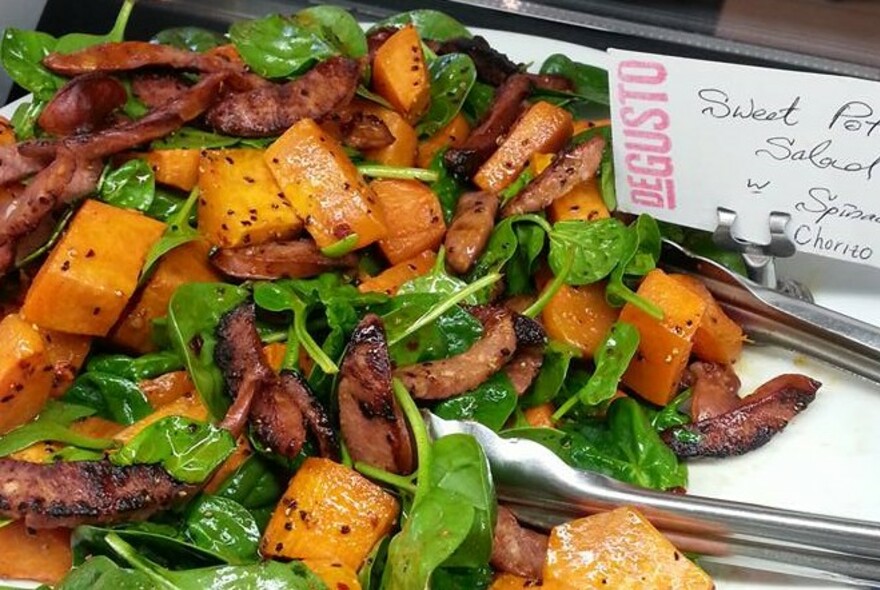 Silver tongs in a dish of pumpkin, greens and fried meat.