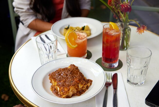 A plate of lasagne on a restaurant table with cocktails.