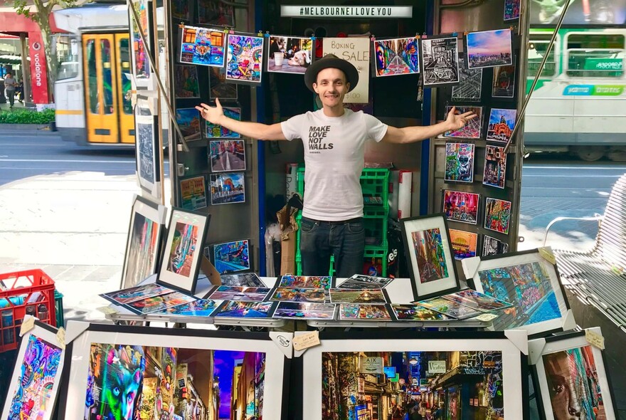 Chris Cincotta standing in front of his street stall surrounded by framed prints of his photographs.