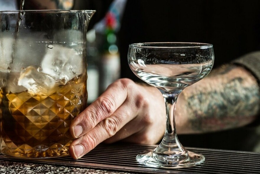Bartender's hands mixing a drink in a jug with an empty glass alongside.