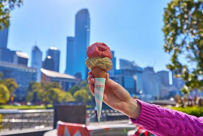 Person holding an ice cream, with a cityscape in the background.